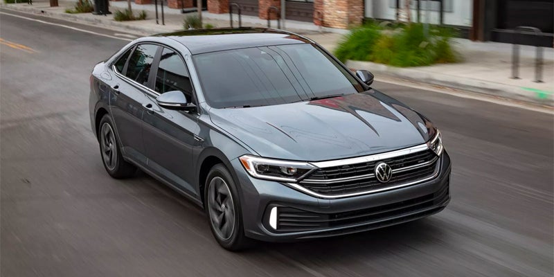 An image of a platinum gray metallic 2024 Volkswagen Jetta driving down the street.