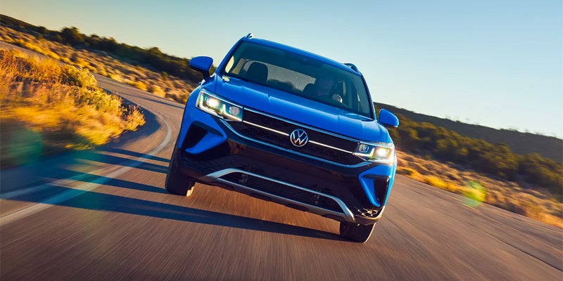 Right-angled photo of a Blue 2024 Volkswagen Taos driving along a curved country road, heading towards the camera.