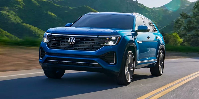 A blue 2024 Volkswagen Atlas Cross Sport driving along the highway, backed by mountains. 