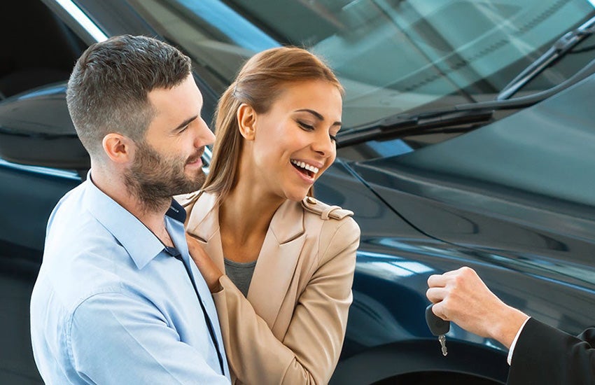 A young couple being handed the keys to their brand new car. 